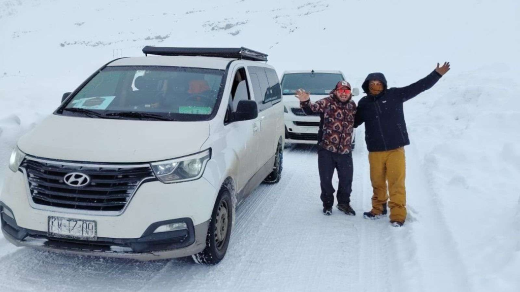 Van de ProTransfer detenida en la nieve junto a otro vehículo, con pasajeros abrigados en la ruta a la cordillera